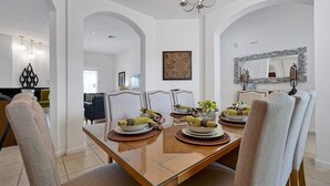 Un comedor con una mesa de vidrio, sillas tapizadas en tono beige y una araña.
