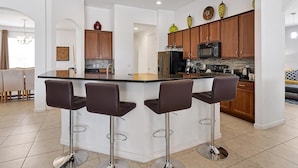 Una cocina moderna con una isla central, taburetes de bar, armarios de madera y un microondas.