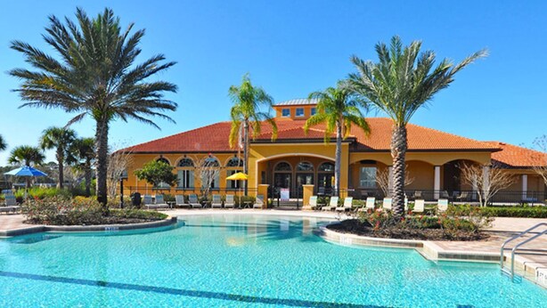 Un resort con piscina, palmeras y un edificio amarillo con ventanas de arco.