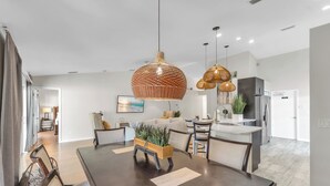 Una cocina moderna con zona de comedor, que incluye una mesa de madera oscura, sillas y una lámpara colgante.
