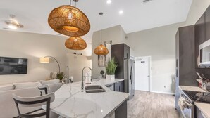 Una cocina moderna con una isla de mármol, electrodomésticos de acero inoxidable y lámparas colgantes de mimbre.