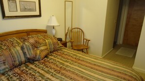 Un dormitorio con una cama, una silla, una lámpara y dos cuadros en la pared.