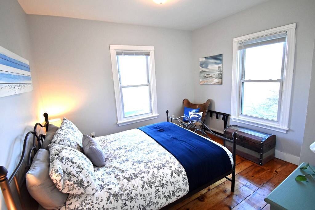 A bedroom with a bed, a nightstand, a chair, a window, and a painting on the wall.