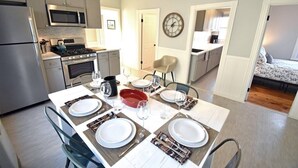 A compact kitchen with modern appliances, a dining area with a table set for four, and a visible bedroom with a bed. - Convenient, Modern Thompson s Point 3-Bed Flat (Portland)