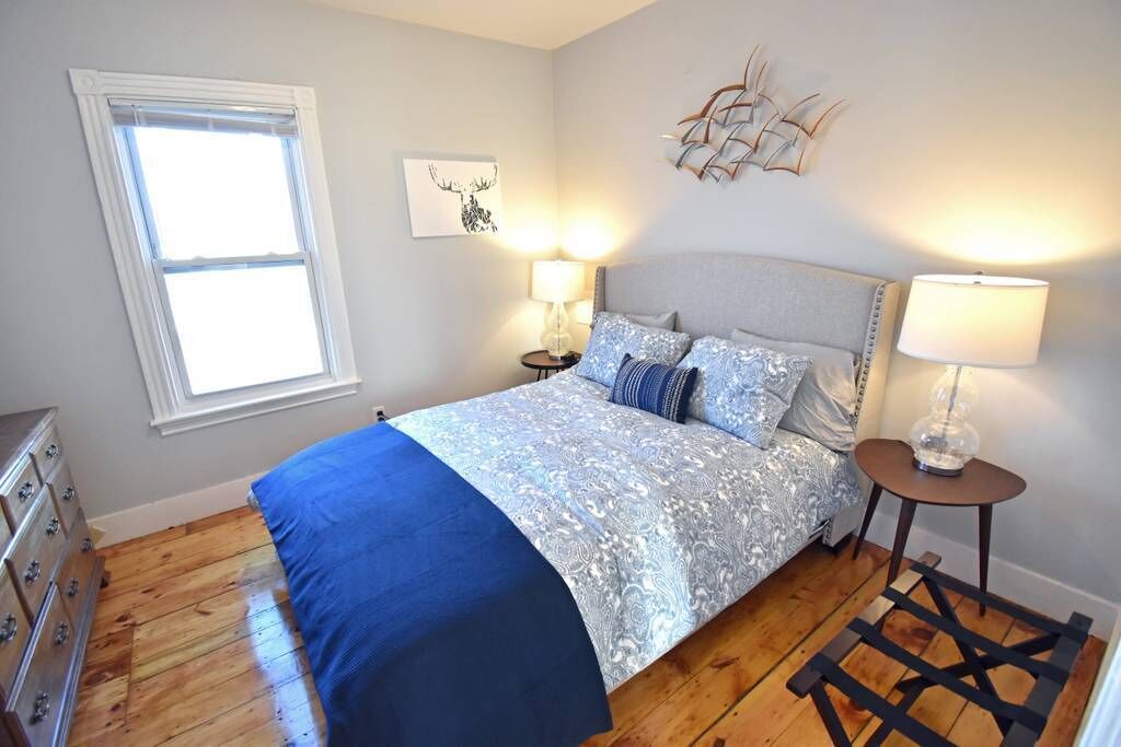 Une chambre à coucher comprenant un lit, deux tables de chevet avec des lampes, une commode, une fenêtre et une œuvre d’art murale.