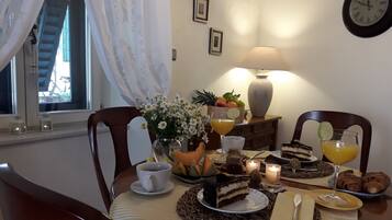 Una mesa de comedor dispuesta con comida, bebidas y velas, con una ventana y cortinas al fondo.
