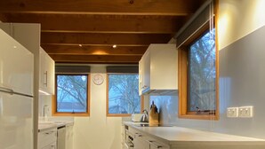 A modern kitchen with white cabinetry, a wooden ceiling, and large windows. - Echo Base – Alpine Family Retreat, Dinner Plain (Dinner Plain)