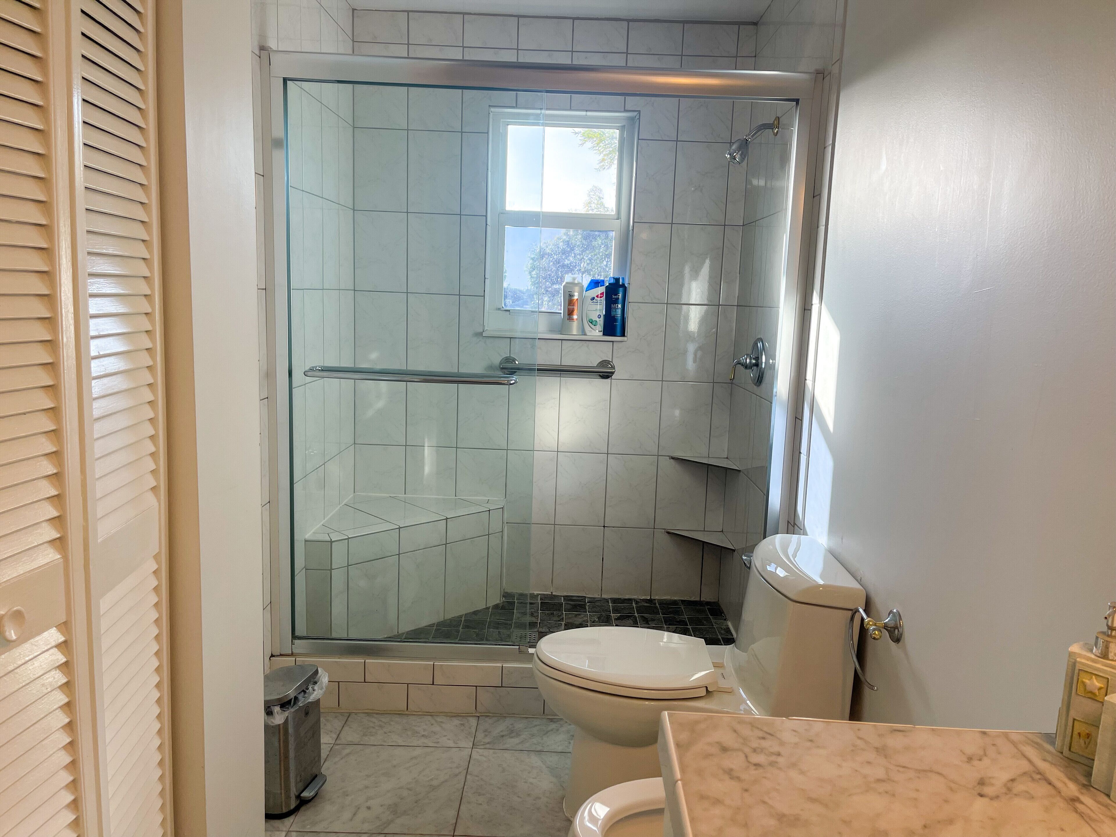 A bathroom with a glass-enclosed shower, a toilet, and a marble countertop.