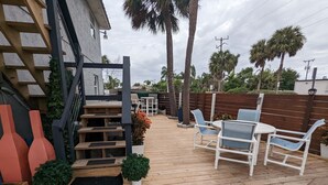 Una terraza de madera con mobiliario exterior, una escalera y vistas del entorno.
