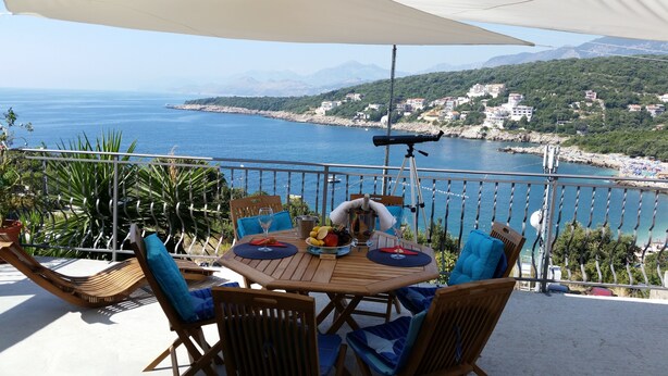Eine Terrasse mit Essplatz, mit Blick auf eine Küstenstadt und das Meer.