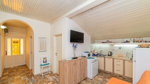 Eine kleine Küche mit einer Mikrowelle, Spüle und Schränken, ein kleiner Tisch mit einer Vase und ein an der Wand montierter Fernseher.
