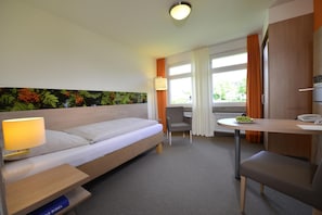 Habitación de hotel con cama, escritorio, silla, lámpara y ventana con cortinas.