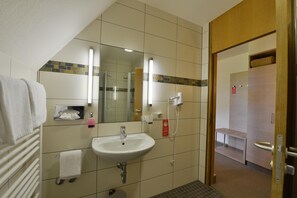 A bathroom with a sink, mirror, towel rack, and a shower area. - Tagungszentrum Schmerlenbach (Hoesbach)