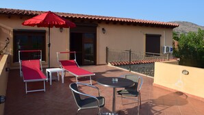 Una terraza con sillones reclinables rojo y blanco, una mesa y un paraguas rojo.