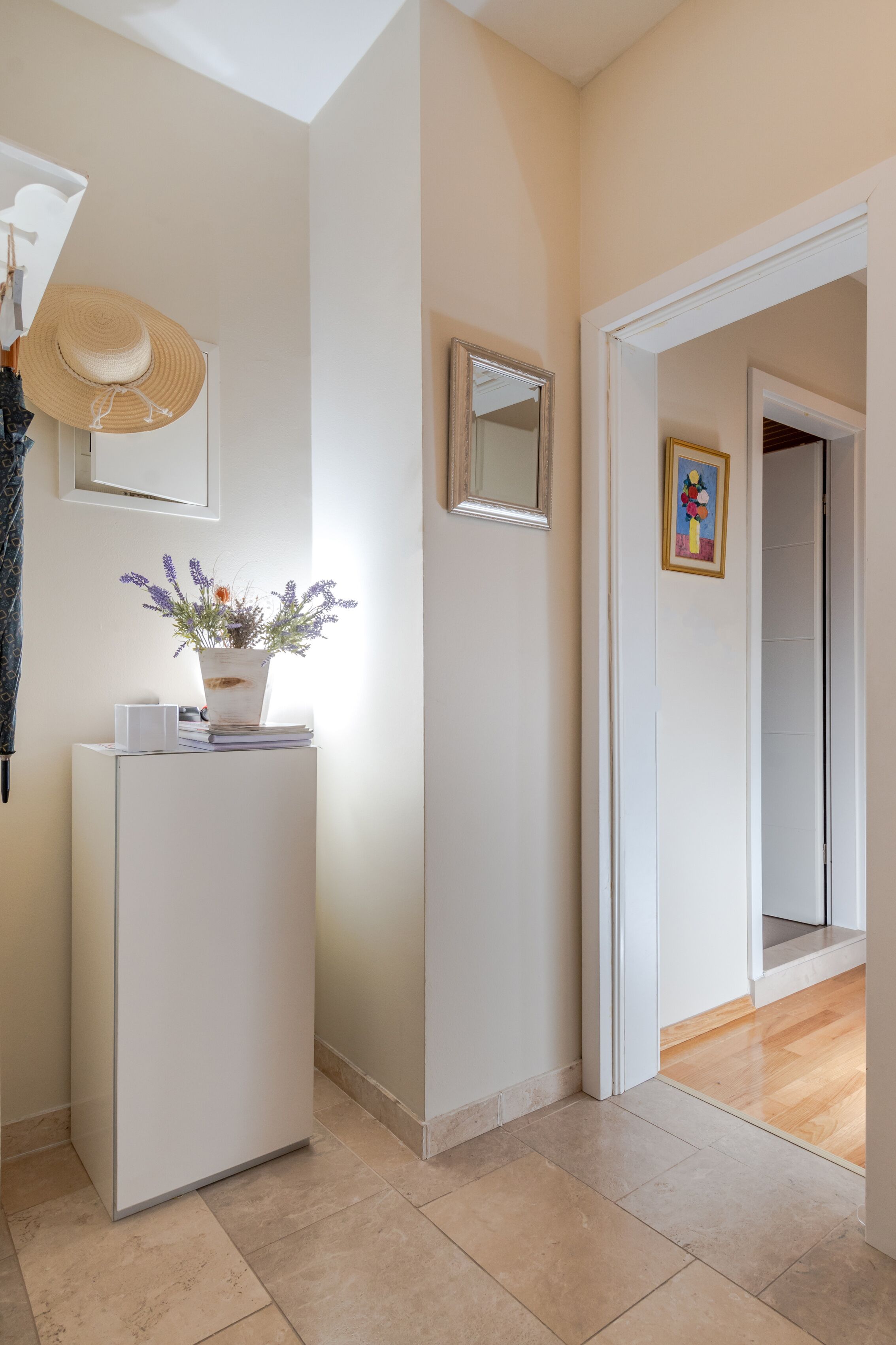 Ein Flur mit einer weißen Tür, einem kleinen Tisch mit einem Topfpflanzen, einem Spiegel und einem gerahmten Bild an der Wand.