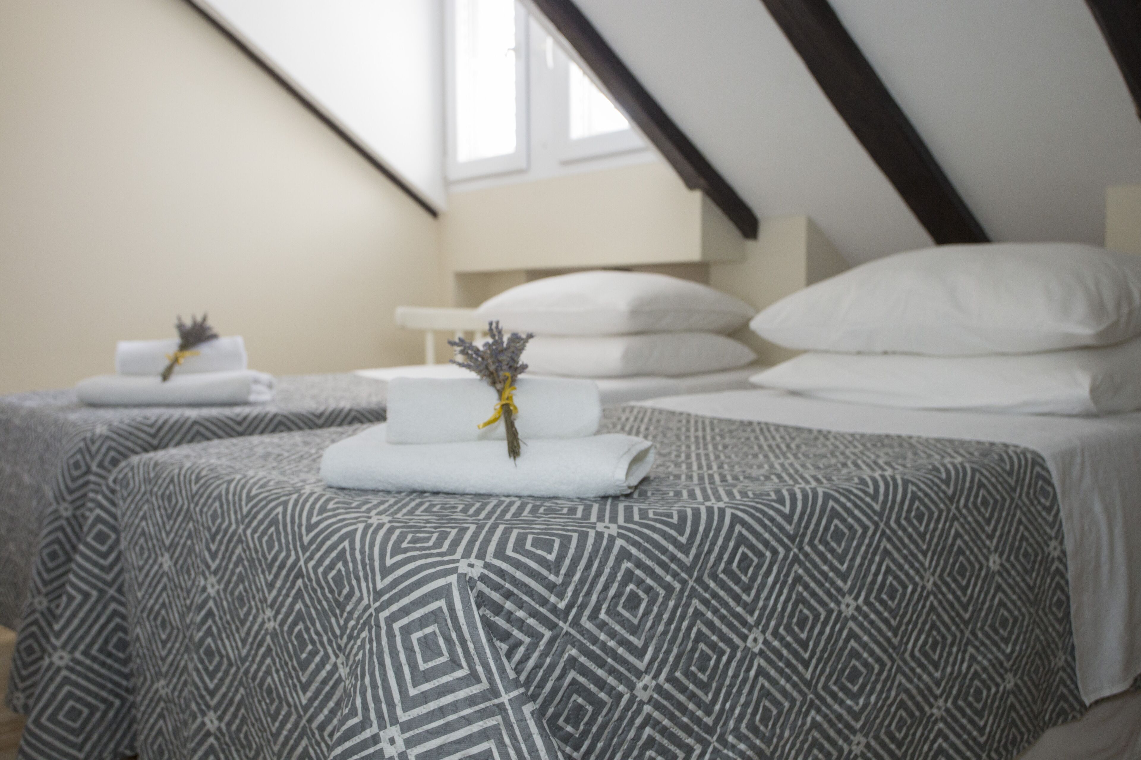 A neatly made bed with patterned bedding, a bedside table with a vase of flowers, and a window with a view of the outside.