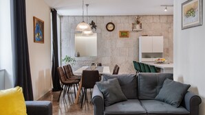 A modern living room with a grey sofa, dining area with chairs, a kitchen area, and a stone wall. - How To Live Better In Split, Apartment  (Split)