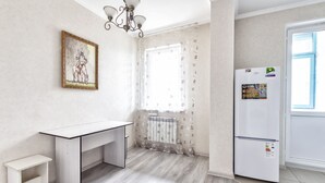 Et moderne køkken med et hvidt køleskab, et lille hvidt skrivebord og et vindue med lette gardiner.