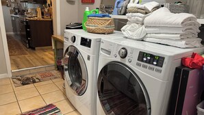 Un espace buanderie comprenant deux machines à laver à chargement frontal, un panier en osier et une pile de serviettes pliées.