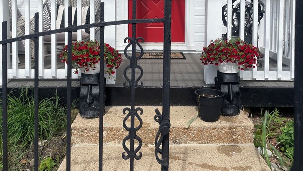 Une maison avec une porte rouge, une pancarte indiquant «Bienvenue» et des marches numérotées menant à l’entrée.