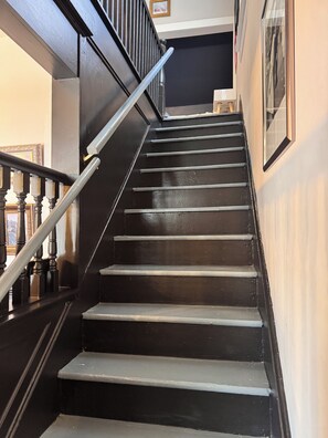 Una escalera con escalones negros y barandilla de metal que conduce a un piso superior.
