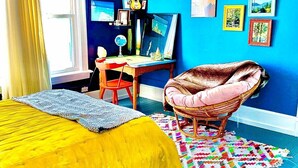 Une pièce comprenant un lit, une chaise, un bureau et des œuvres d’art accrochées aux murs.