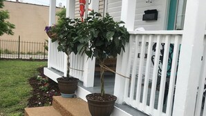 Une véranda blanche agrémentée d’un arbre en pot et de jardinières suspendues.