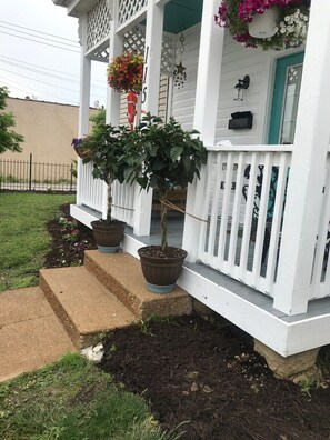 A white porch with a potted tree and hanging flower baskets.