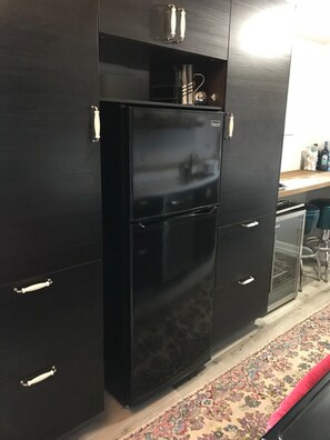 A kitchen with a black refrigerator, a wooden countertop, and a patterned rug.