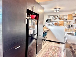 Een moderne keuken met donkere kastjes, een inbouwkoelkast en diverse keukengerei en pannen aan de muur.