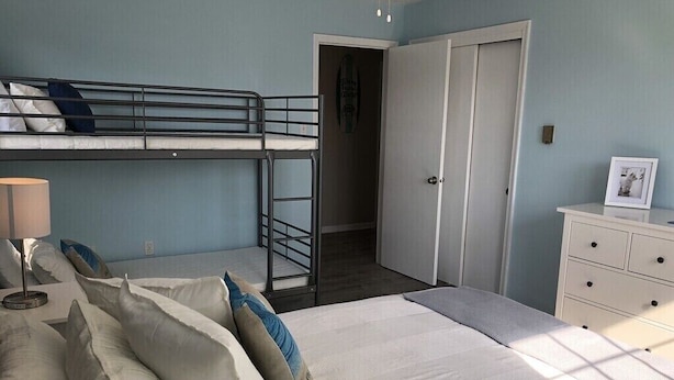 Een slaapkamer met stapelbedden, een nachtkastje met lamp, een dressoir en een deur naar een andere kamer.