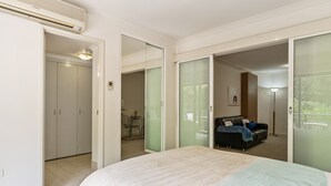 Ein Schlafzimmer mit einem Bett, einem Kleiderschrank, einer Glasraumtür, die auf einen Balkon führt, und einem kleinen Tisch mit Stühlen.