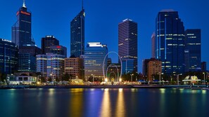 A city skyline with modern high-rise buildings, including a prominent hotel with a distinctive circular light feature in the foreground. - Balcony, bath, kitchen, laundry, pool, tennis court, gym, designated car bay (Perth)