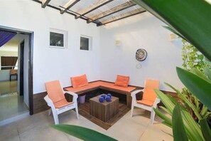 A cozy outdoor seating area with a wooden table and orange cushions, surrounded by white chairs.