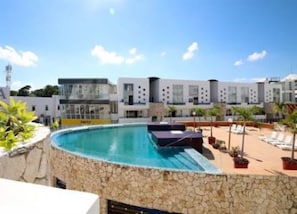 A pool area with a stone wall, lounge chairs, and a modern building in the background.