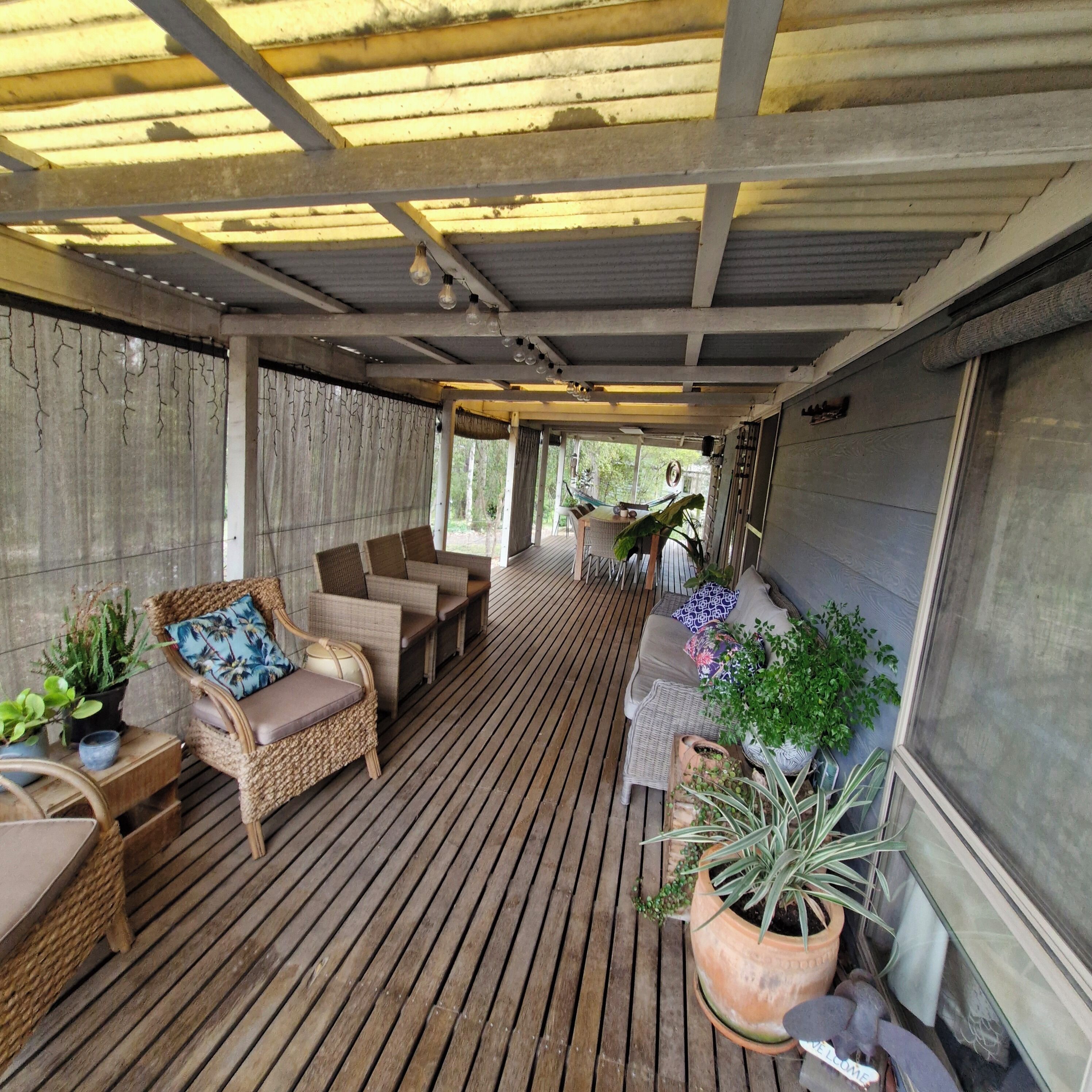 Un espacio de estar al aire libre con techo, mobiliario de mimbre y plantas en macetas.