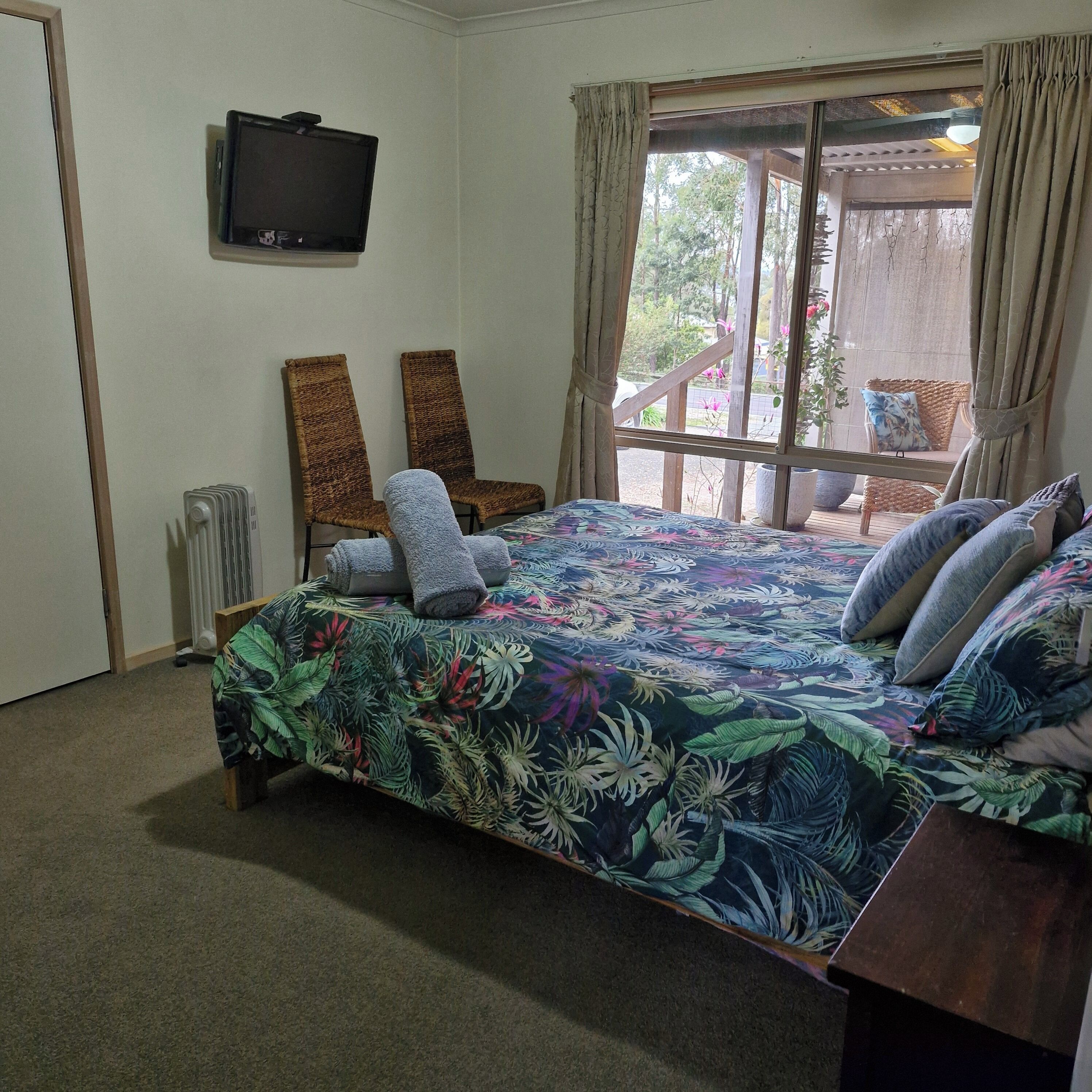 Un dormitorio con una cama, dos sillas, un televisor y una ventana con cortinas.