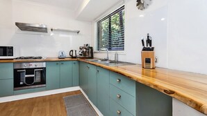 A compact kitchen with teal cabinets, a wooden countertop, a built-in oven, a microwave, a kettle, and a knife block. - Mahogany Lodge - townhouse near Tallow Beach (Byron Bay)