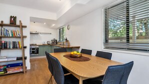 A modern kitchen with a dining area, wooden furniture, and a window with blinds. - Mahogany Lodge - townhouse near Tallow Beach (Byron Bay)