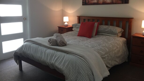 A neatly made bed with a blanket and a rolled towel, a wooden headboard, a bedside table with a lamp, and a painting on the wall. - Family Friendly, light & bright ideal for short or longer stays (York)
