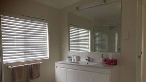 A bathroom with a white vanity, a large mirror, and two windows with blinds. - Family Friendly, light & bright ideal for short or longer stays (York)
