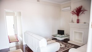 A modern living room with a white sofa, a glass coffee table, a fireplace, and a red vase on the mantel. - Family Friendly, light & bright ideal for short or longer stays (York)