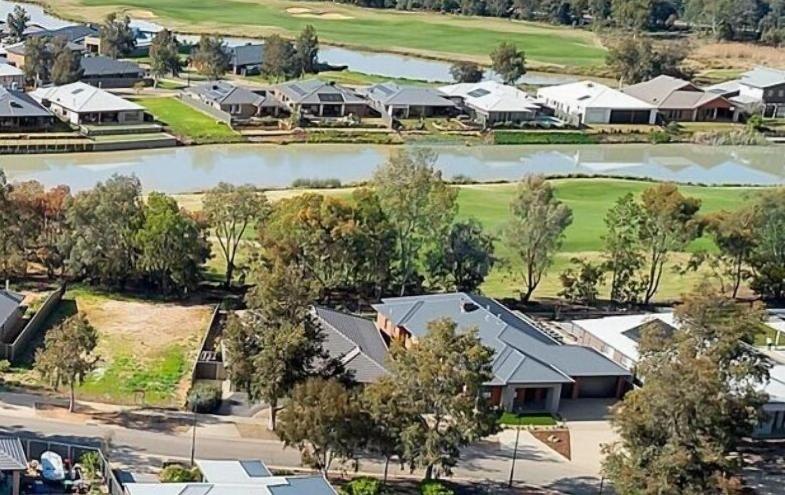 Un barrio residencial con casas, un estanque y un campo de golf al fondo.