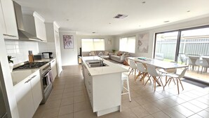 A modern kitchen with white cabinetry, a central island with a sink, and a dining area with white chairs and a table. - Hyland Hideaway Yarrawonga (Yarrawonga)