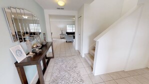 A spacious hallway with a dark wooden console table, a white rug, and a staircase leading to another room. - Affordable 4 bedrooms at Crystal Cove (1527) (Kissimmee)