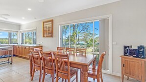 Un vaste espace de salle à manger avec une grande table et des chaises, une cuisine dotée de meubles en bois et une vue sur l’extérieur grâce à de grandes fenêtres.
