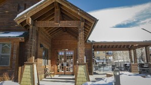 A wooden lodge with a covered entrance, a snow-covered ground, and a patio area with outdoor seating.