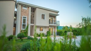 A modern two-story house with a balcony, a stone facade, and a well-maintained garden.