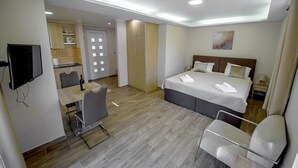 A hotel room with a bed, a desk, a chair, a television, and a kitchenette.