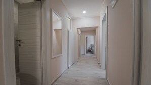 A hallway with light-colored walls and wooden flooring, leading to a bathroom and a bedroom.